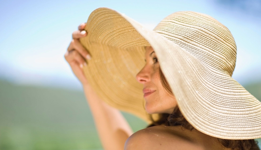 A woman in the sun wearing a big, floppy, straw hat to cover her face.